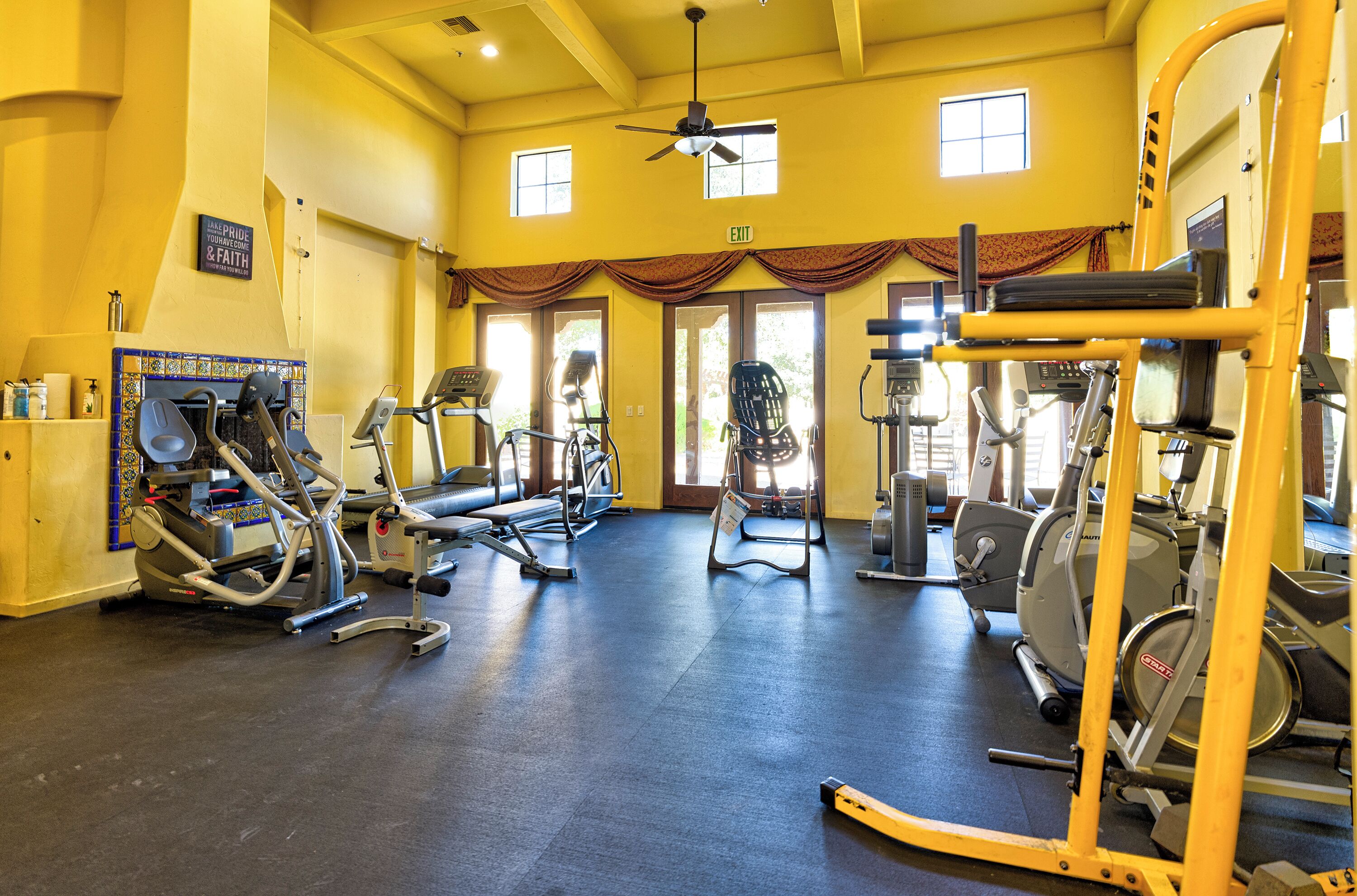 A gym with various exercise equipment, large windows, and a ceiling fan.