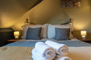 Una cama bien hecha con almohadas, una lámpara a cada lado y toallas enrolladas sobre la cama.