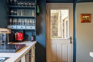 Una cocina con cafetera, una botella de vino y diferentes vasos en estantes.