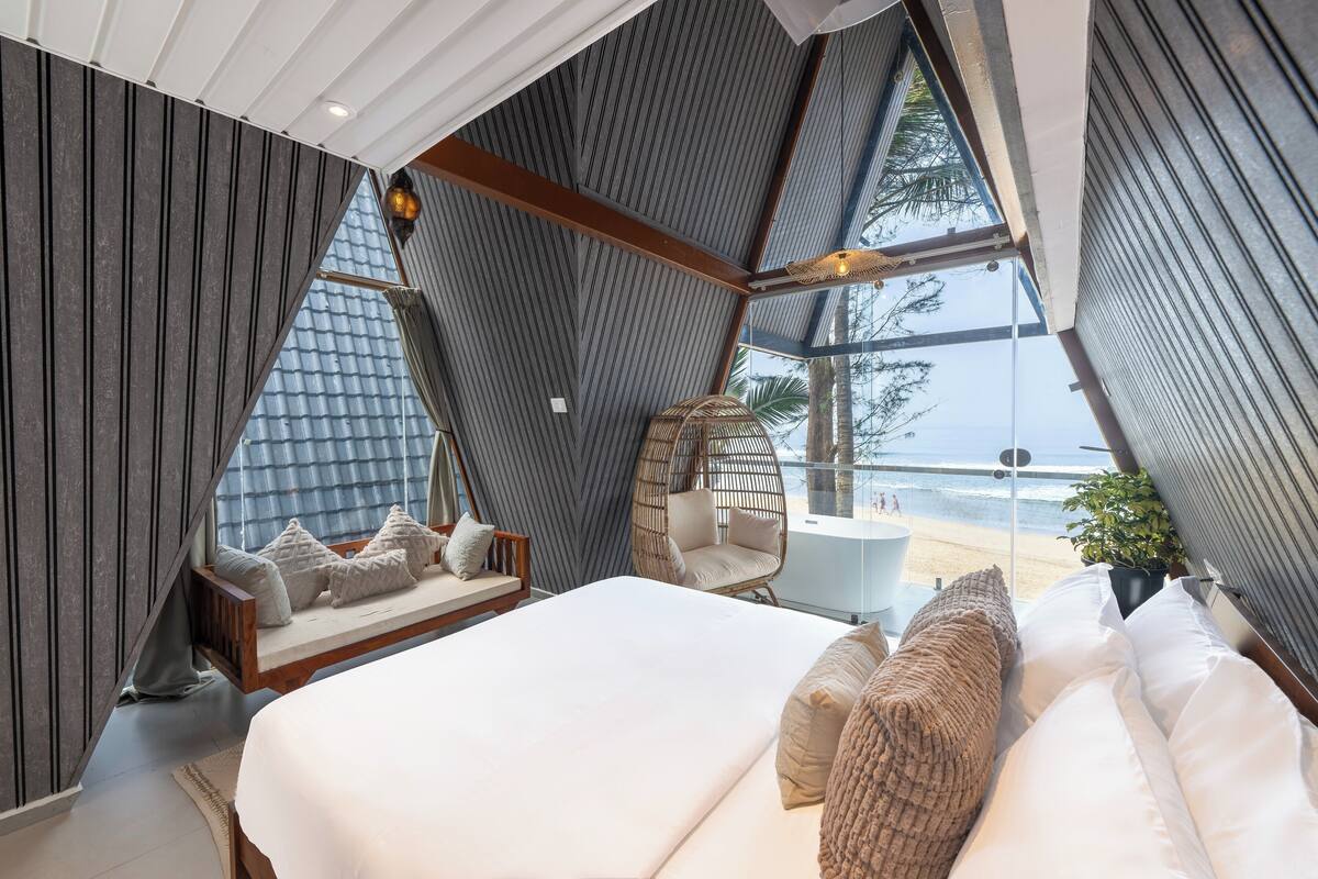 Un dormitorio con una cama grande, una silla colgante y vistas a la playa.