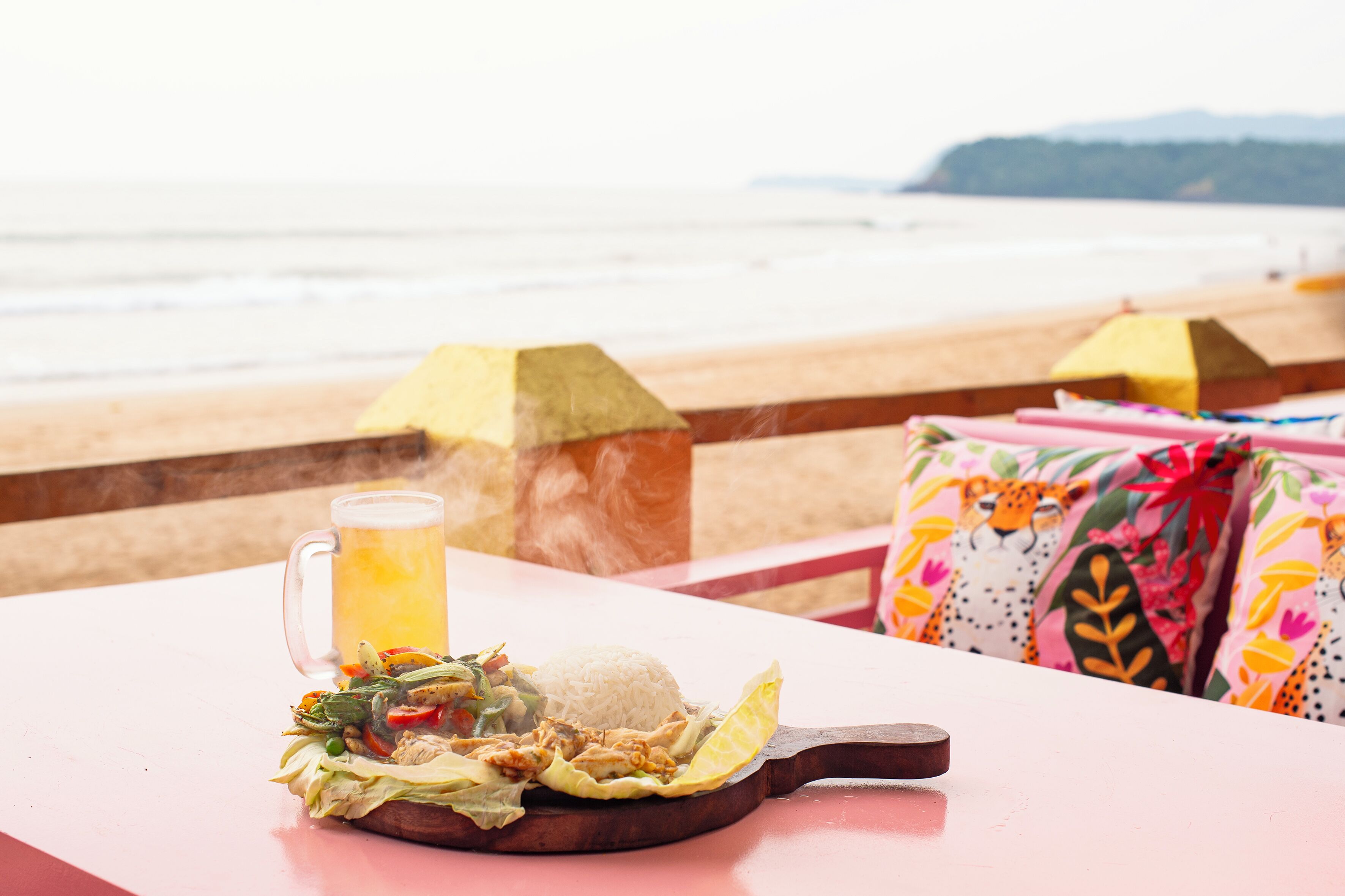 Une table dressée avec un repas, une boisson et une vue sur la plage.