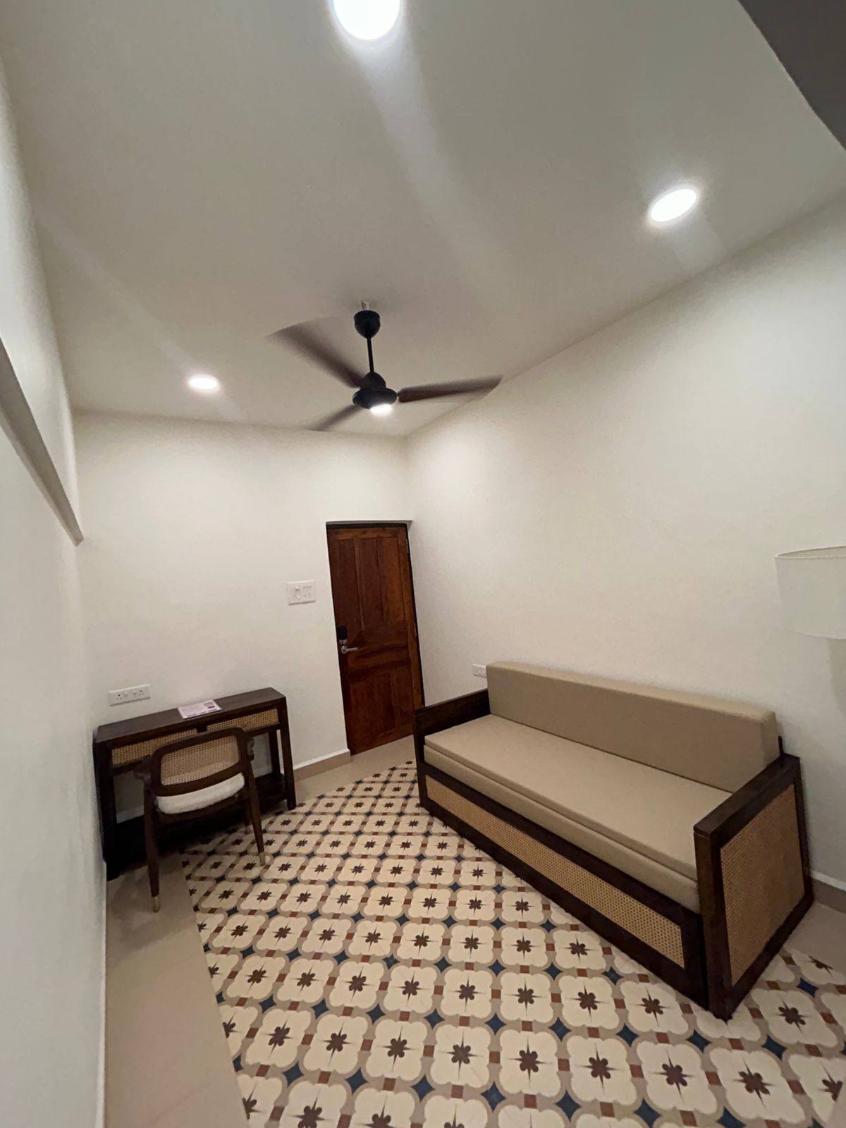 A room with a ceiling fan, a sofa, a small table, and a patterned floor.