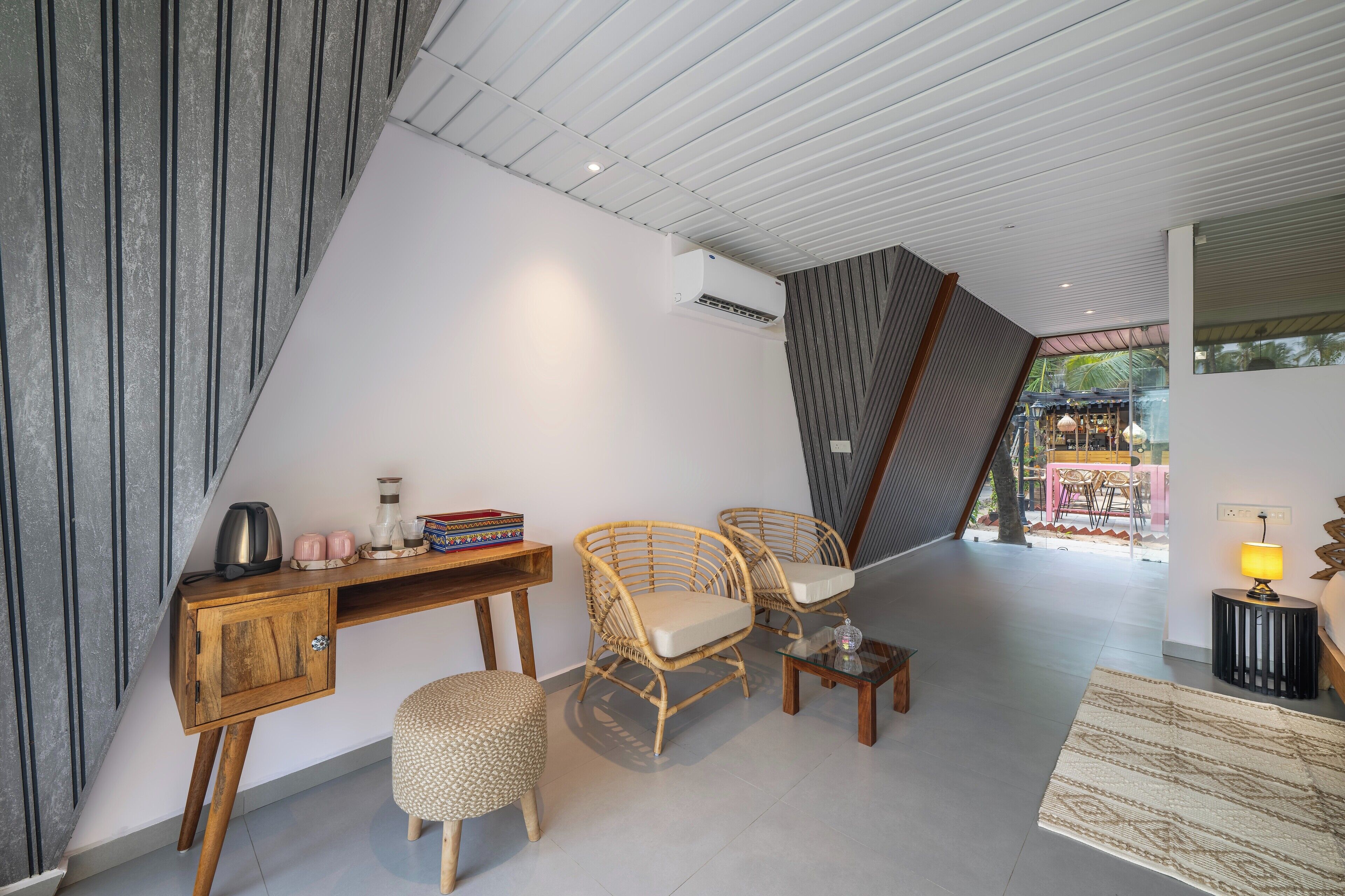 Ein modernes Interieur mit einem Holztisch, zwei Korbstühlen, einem kleinen Hocker und einem Glastisch.