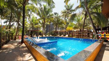 Une piscine rectangulaire dotée d’une terrasse en bois et agrémentée d’un élément décoratif aquatique bleu, le tout entouré de palmiers et de chaises longues.