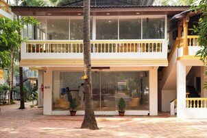 A two-story building with a balcony, potted plants, and a glass entrance.