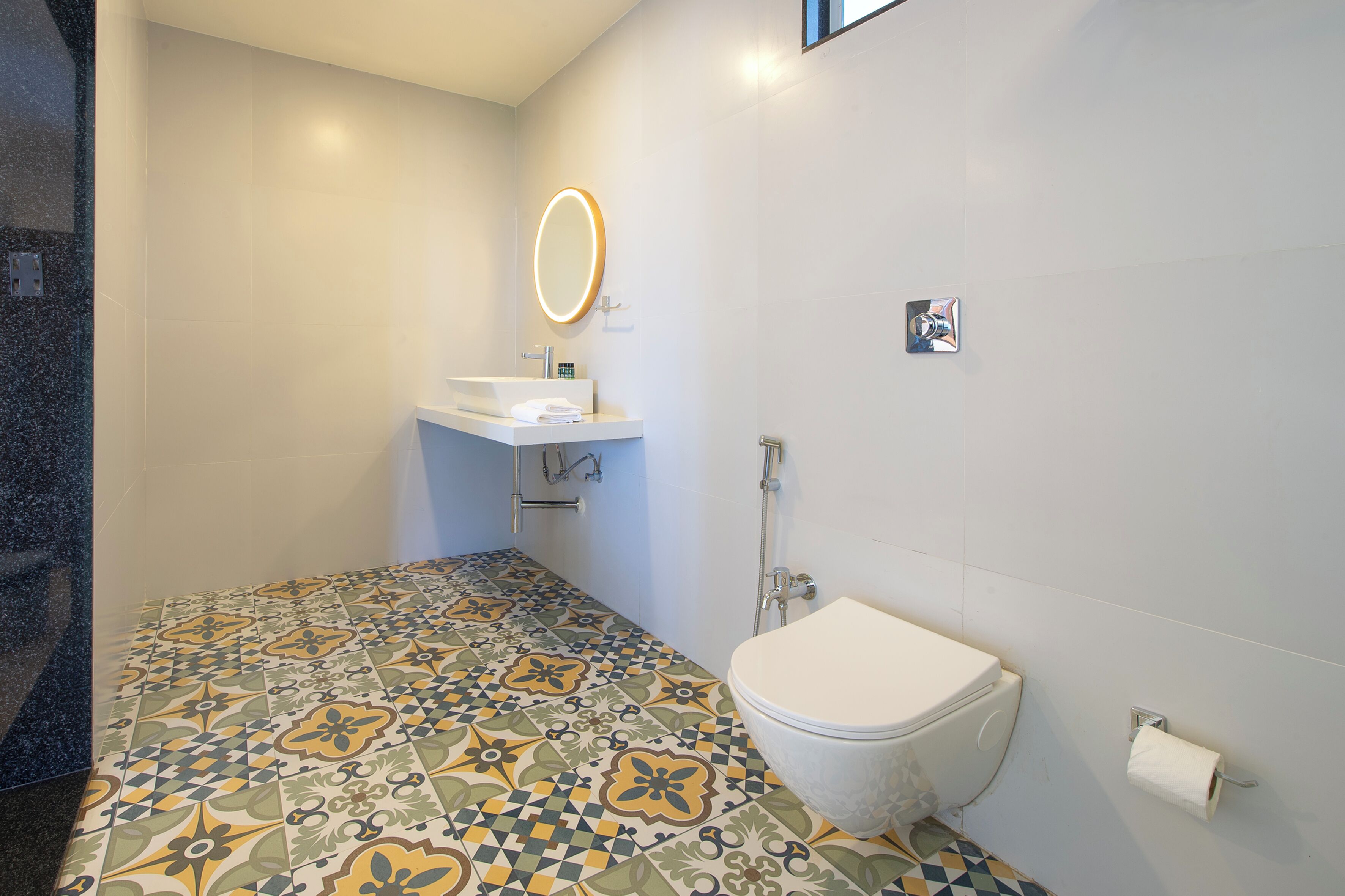 A bathroom with a tiled floor, a toilet, a sink with a mirror, and a towel rack.