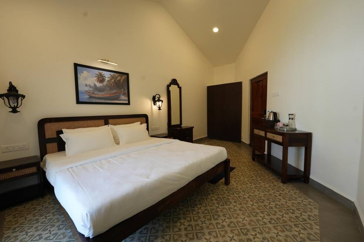 Una habitación de hotel con una cama grande, una mesita de noche, un escritorio con lámpara, un armario y un cuadro en la pared.