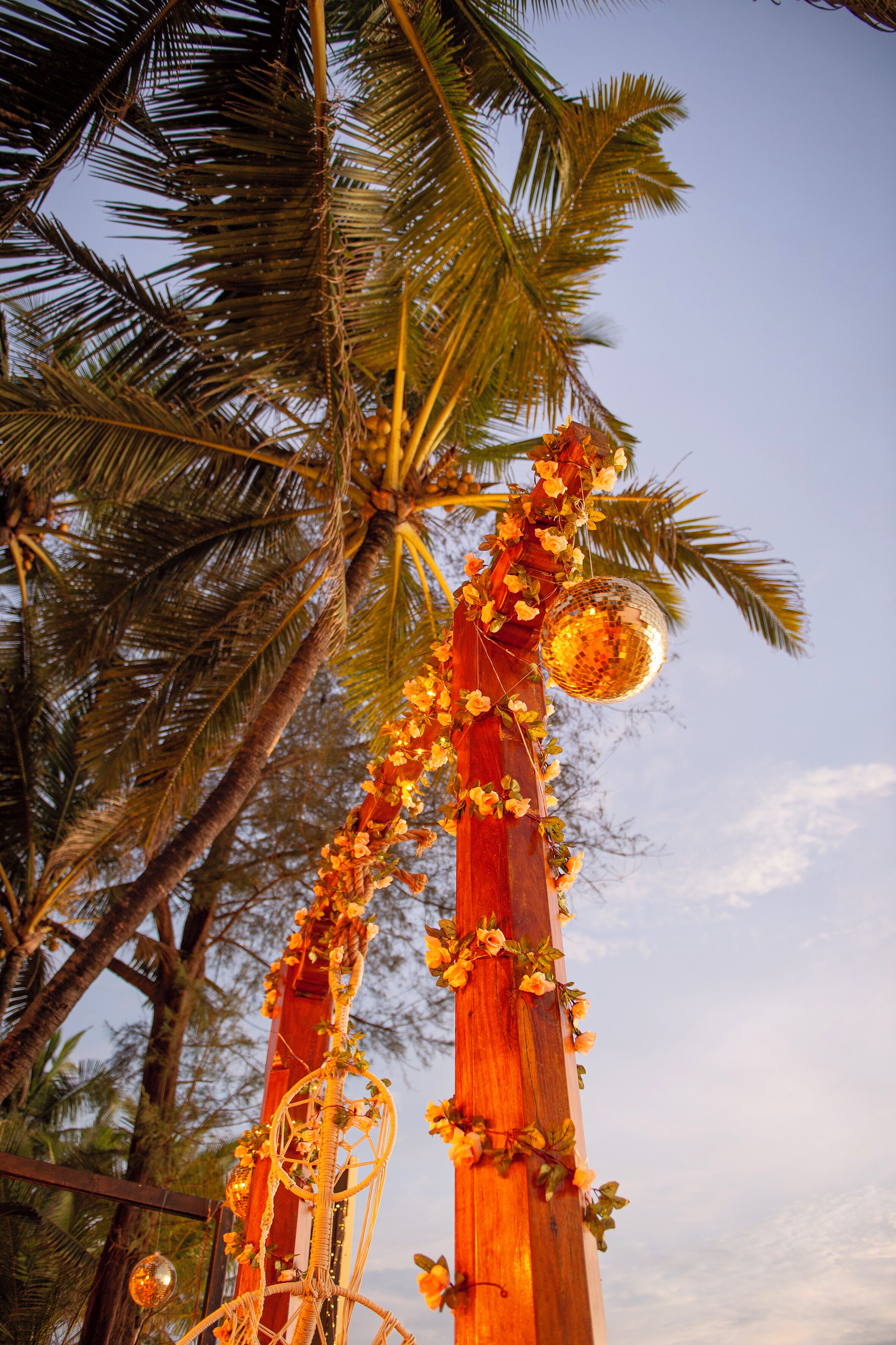A wooden structure adorned with flowers and a disco ball, surrounded by palm trees.