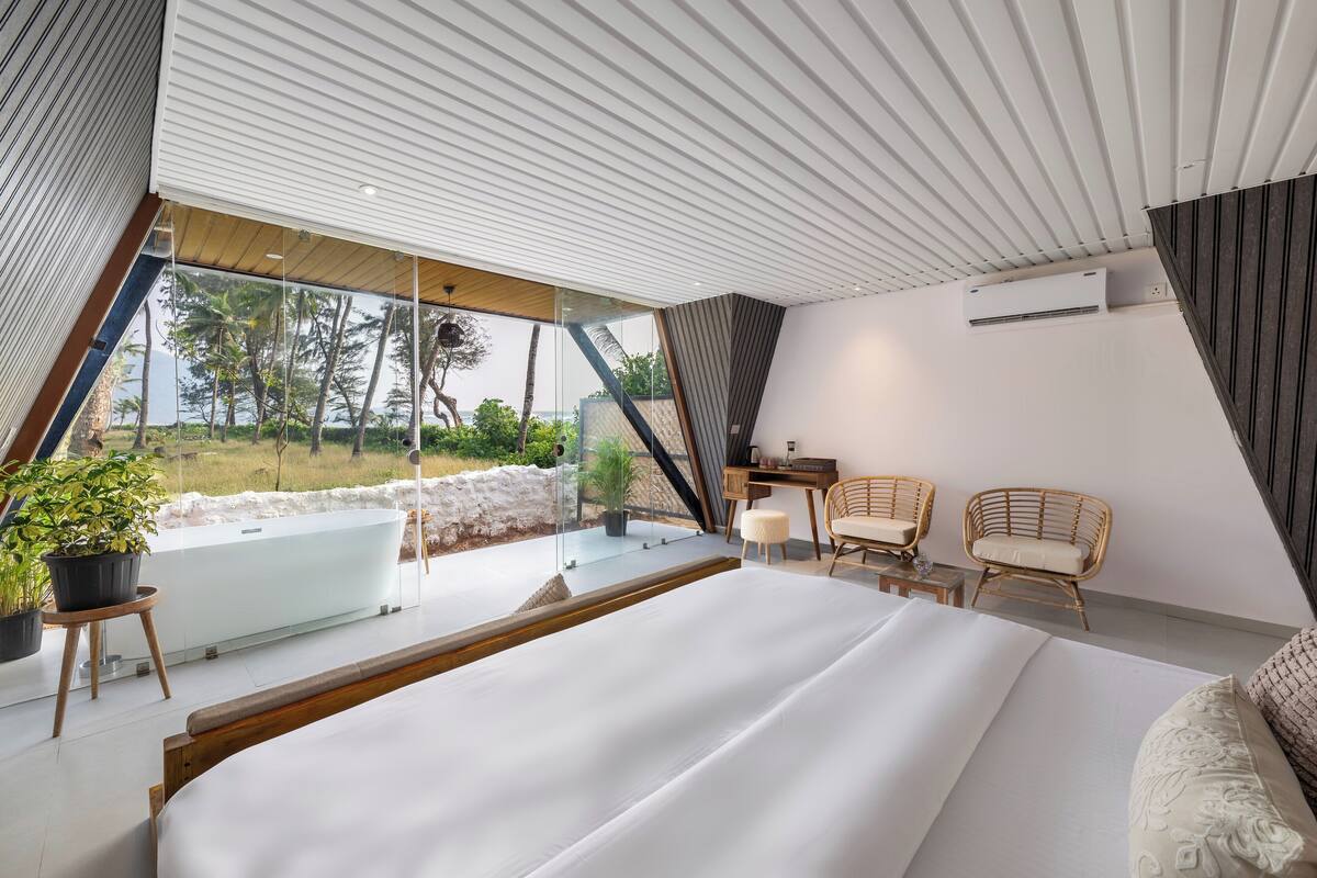 Un dormitorio moderno con una cama grande, una bañera de hidromasaje y sillones de mimbre, con vistas al exterior.