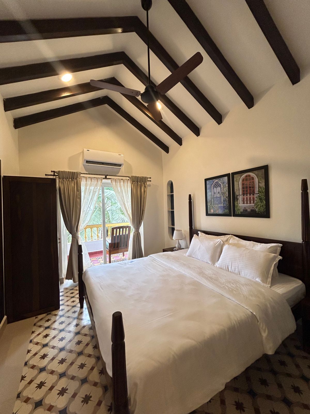 A bedroom with a large bed, wooden ceiling beams, an air conditioning unit, and a view of the outdoors.