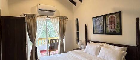 A bedroom with a large bed, wooden ceiling beams, an air conditioning unit, and a view of the outdoors.