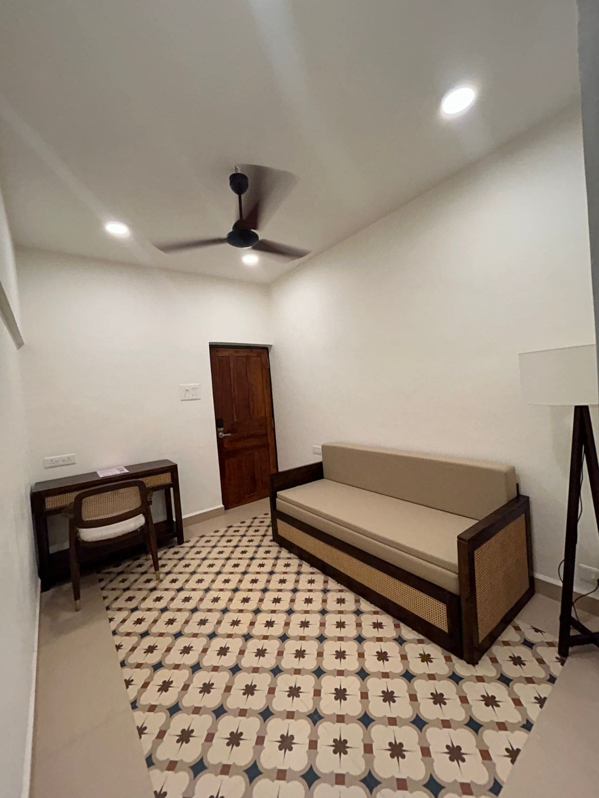 A room with a sofa, a desk, a chair, a ceiling fan, and patterned flooring.