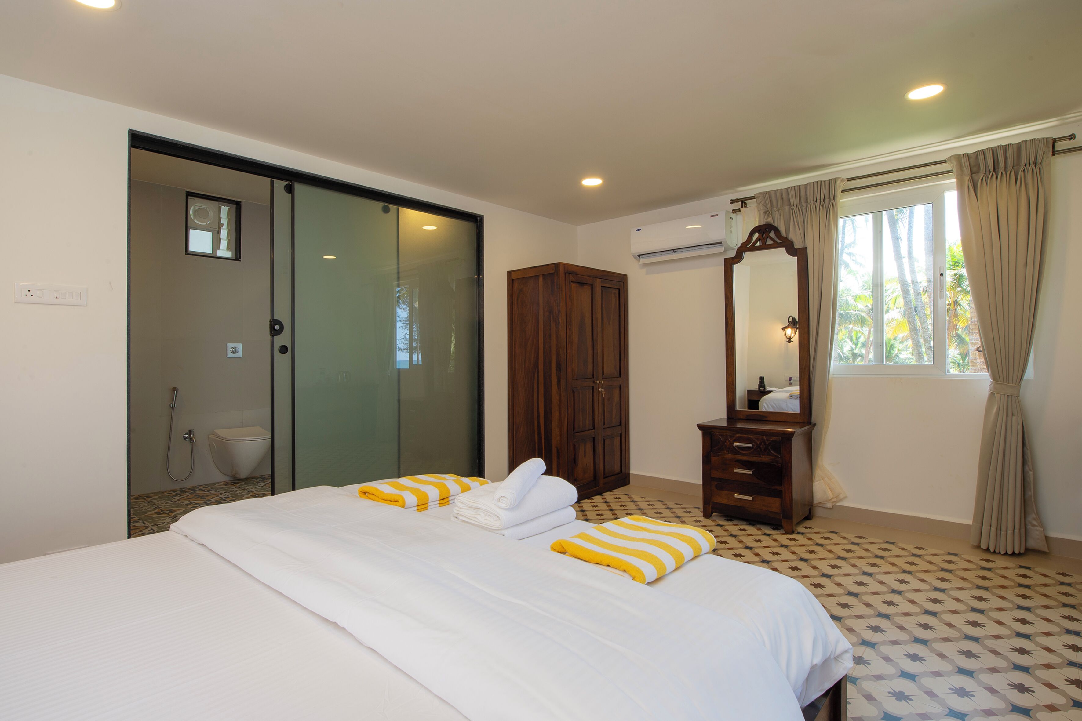 A hotel room with a bed, a wooden wardrobe, a mirror, and a window with curtains.