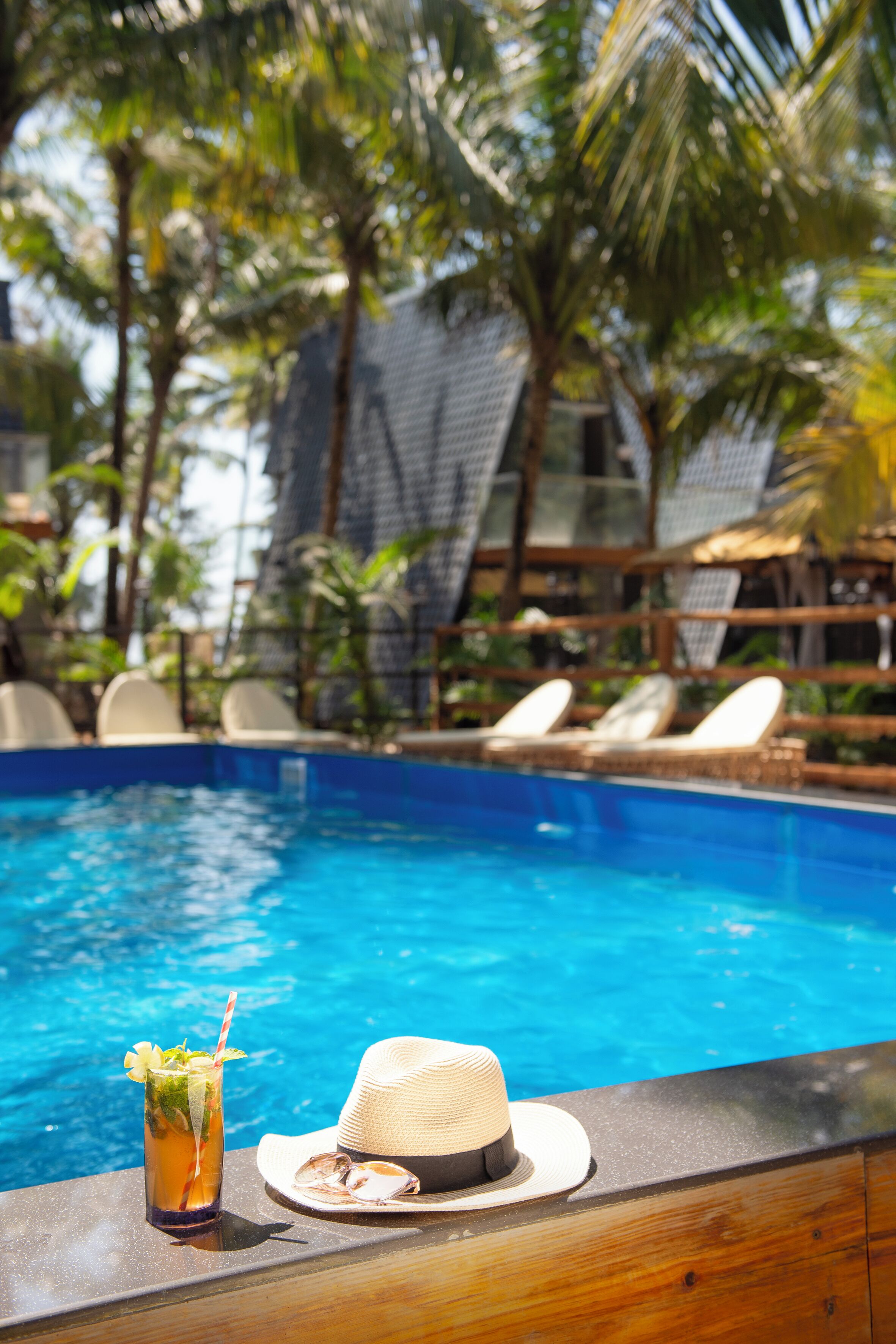 A poolside area with a drink and a hat on a wooden ledge.
