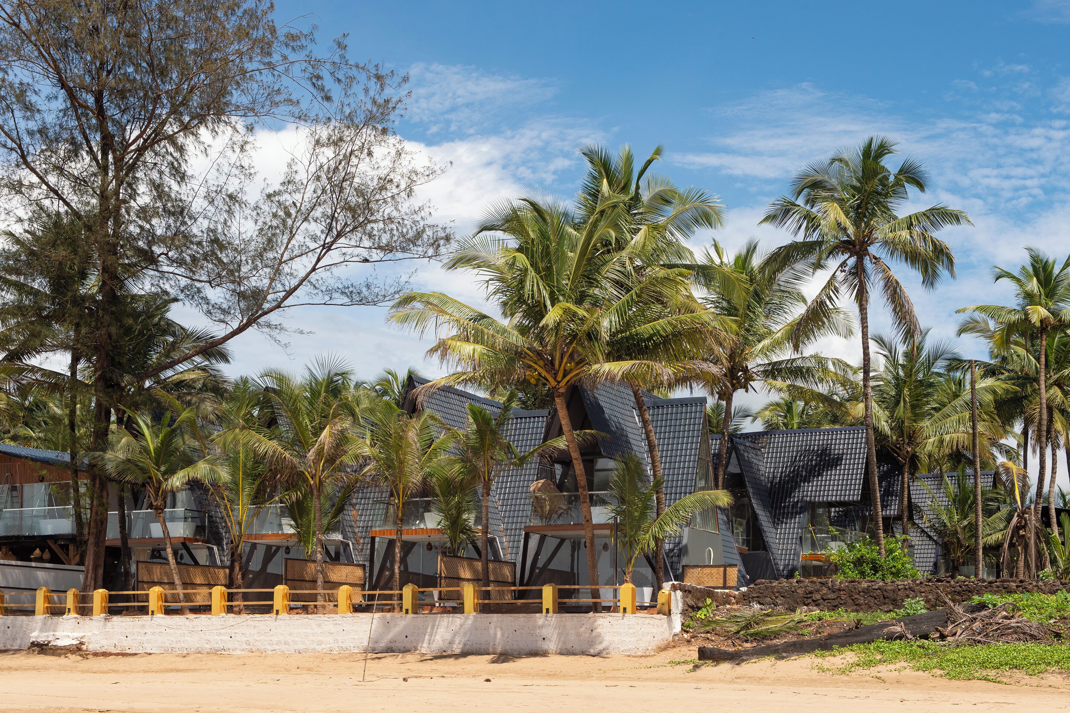 Un hotel frente a la playa con arquitectura moderna, palmeras y una playa de arena.