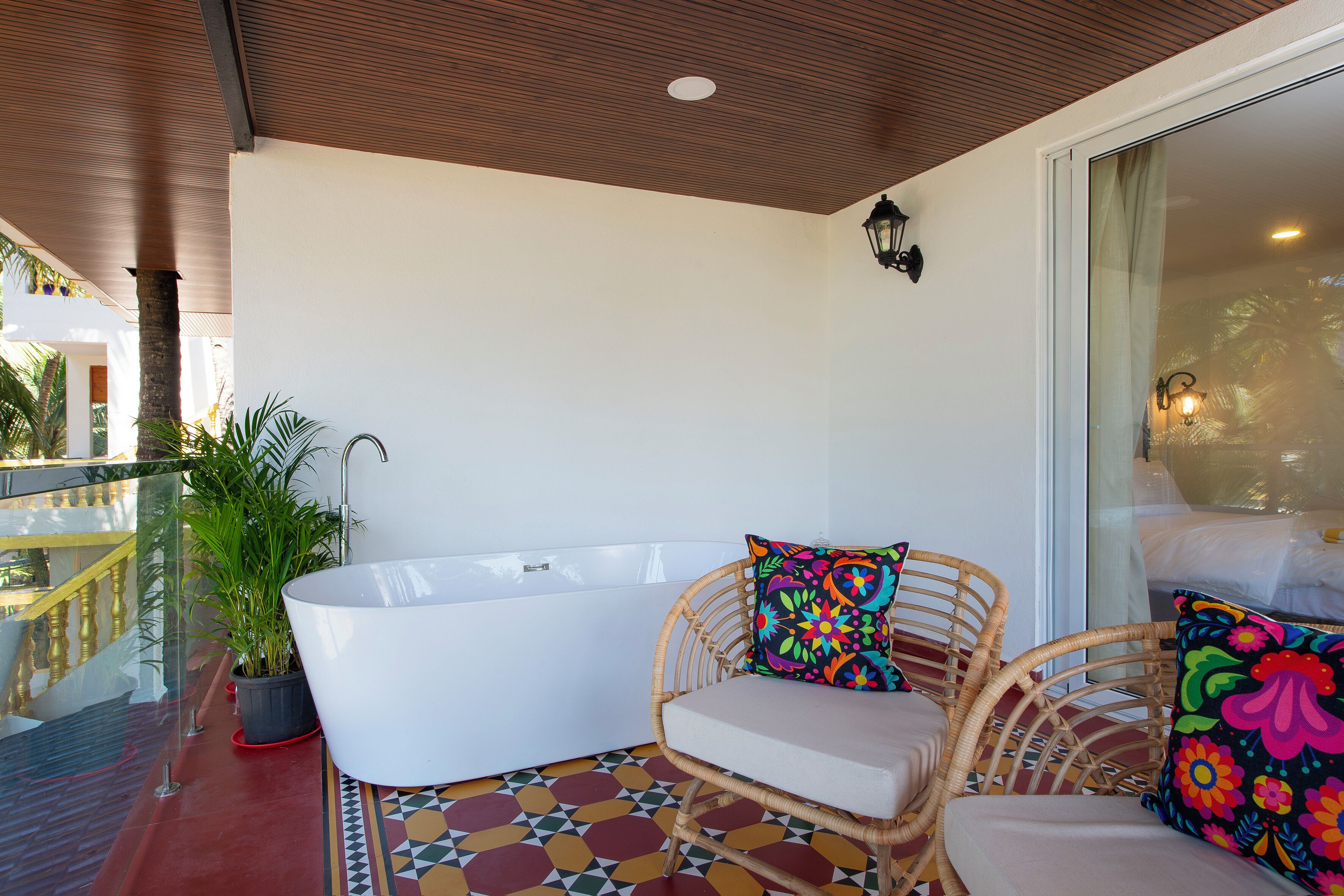 Un balcon avec une baignoire blanche, des fauteuils en osier et une plante en pot.