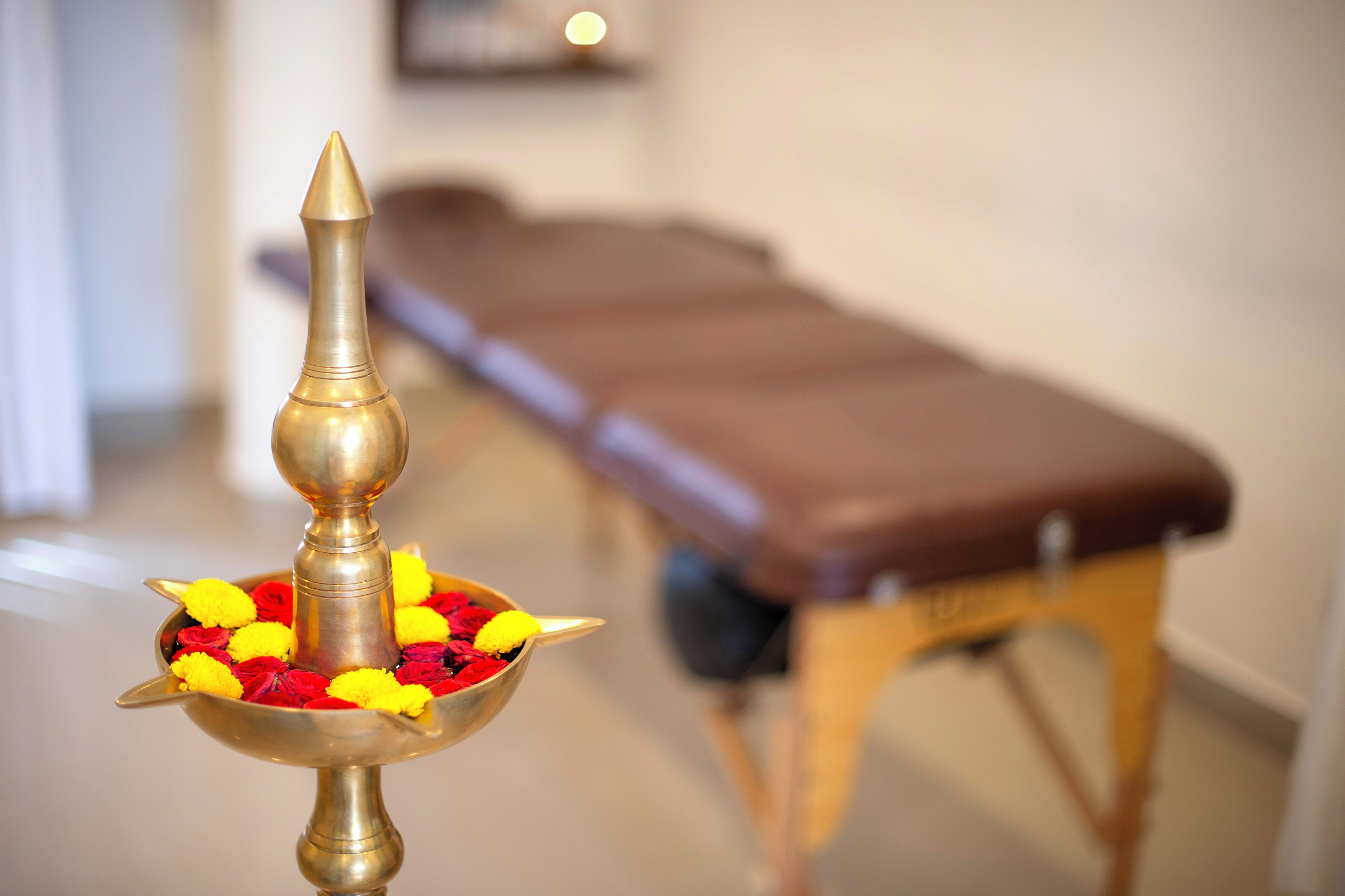 A brass oil lamp with marigold flowers in a room with a massage table.