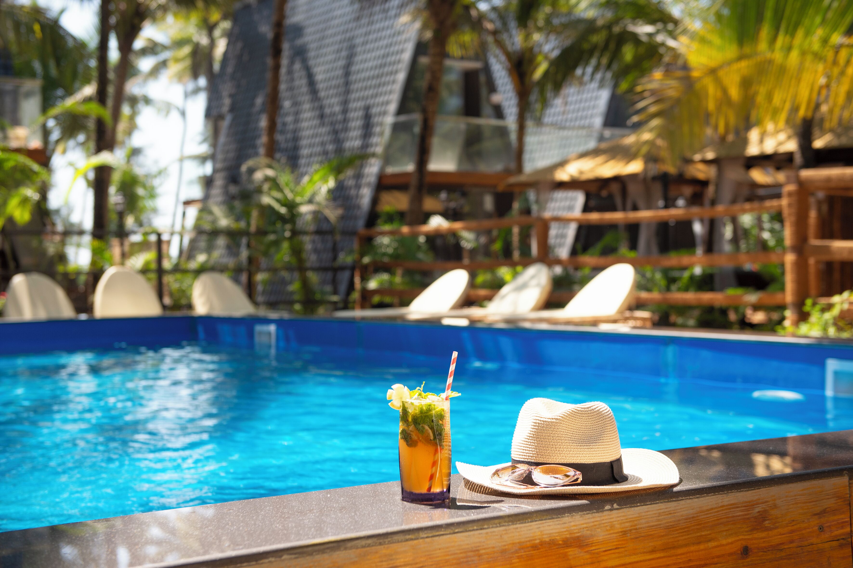A poolside area with a drink and a hat on the edge.