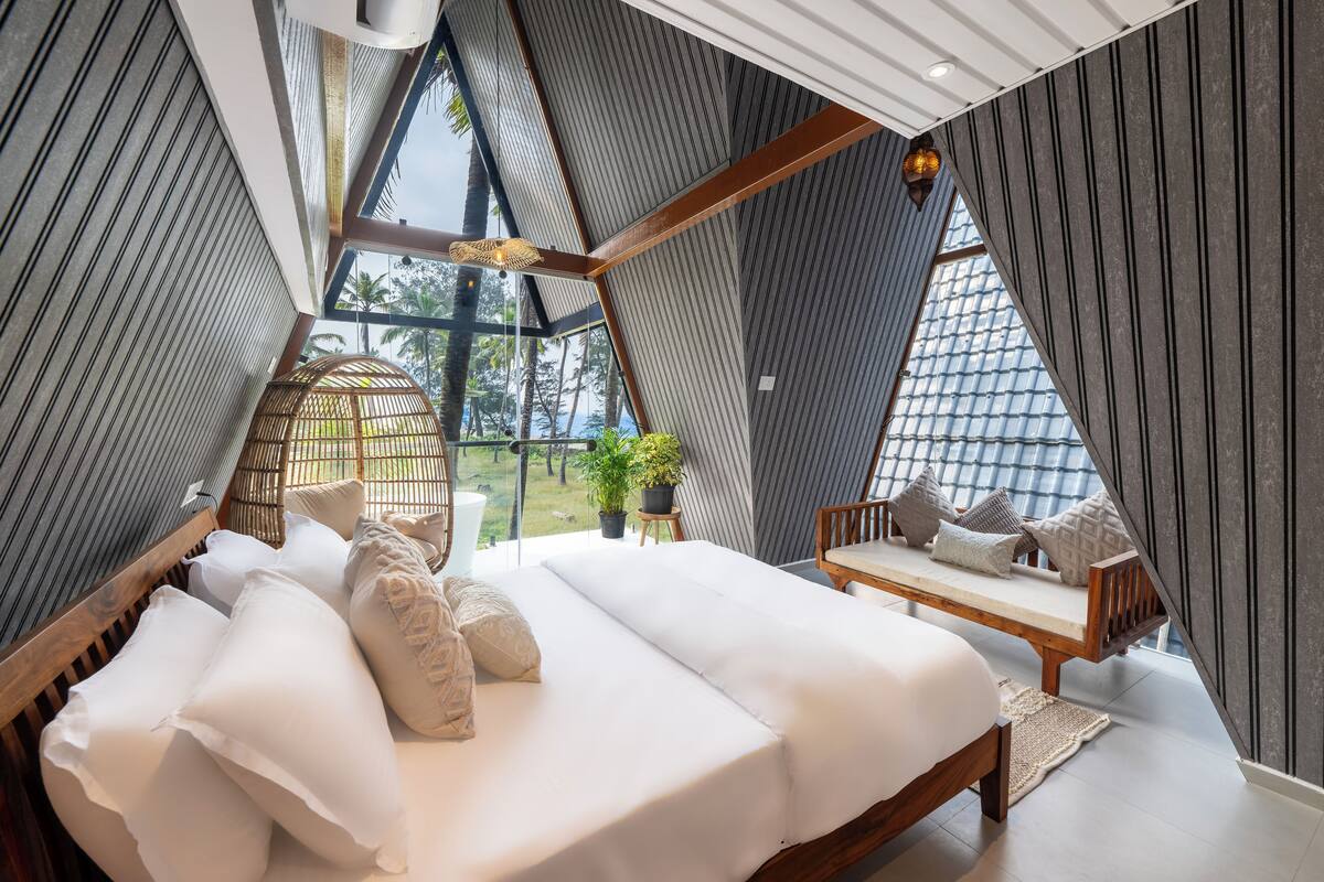 Una habitación moderna de forma triangular con una cama grande, un banco de madera y vistas al exterior.