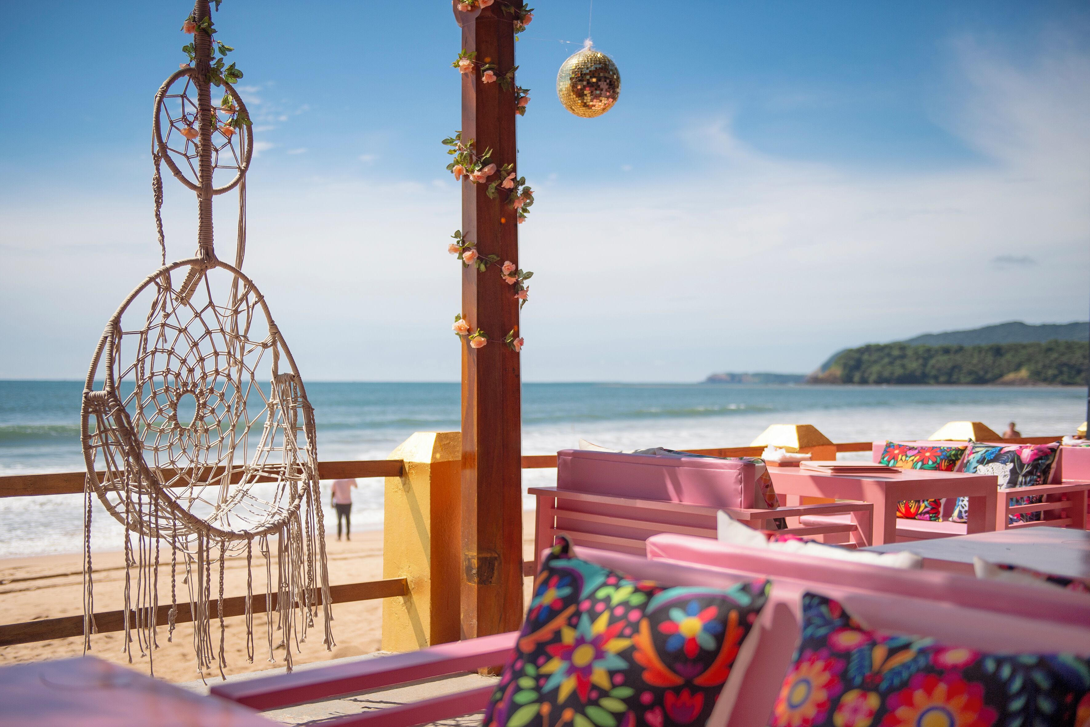 A beachside seating area with a dreamcatcher, a hanging disco ball, and a view of the ocean.