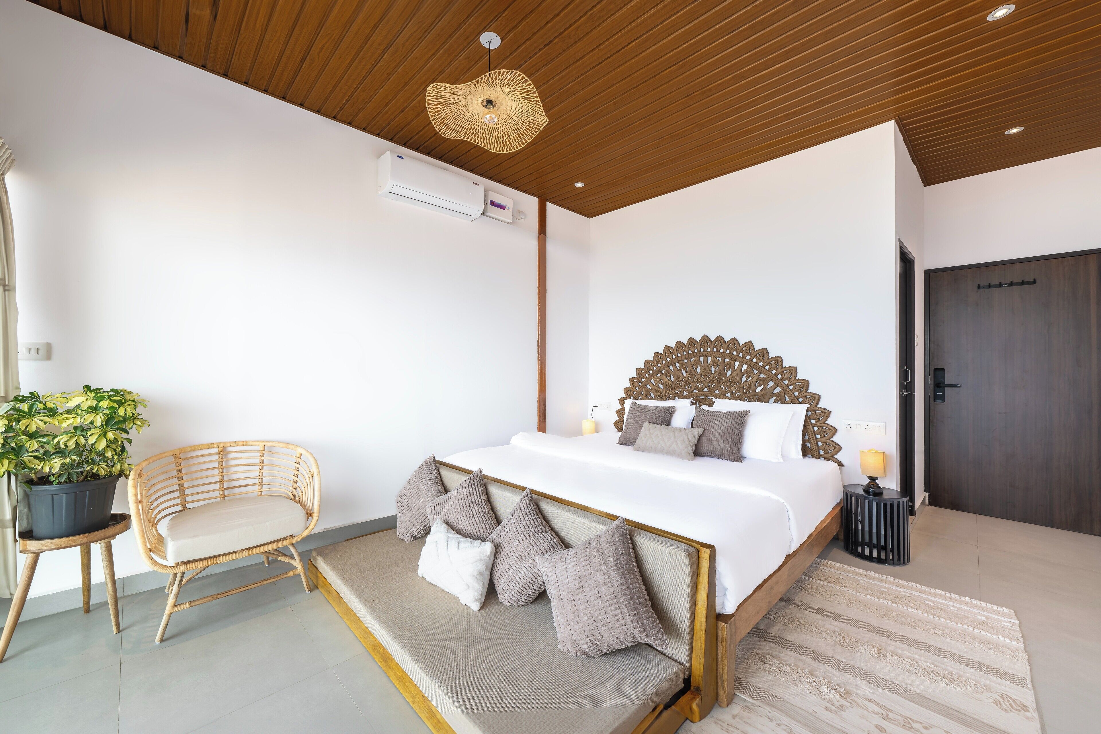 A modern bedroom with a wooden ceiling, a large bed with a unique headboard, a bedside table with a lamp, and a potted plant.
