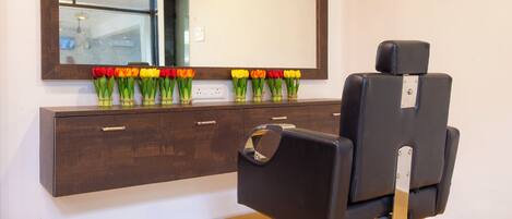 A salon with a mirror, a wooden cabinet with drawers, and a chair.