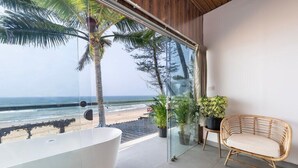 A balcony with a view of the beach, a white bathtub, and a wicker chair. - The Rose Goa Beach Resort (Canacona)