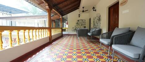 A covered balcony with a colorful geometric floor pattern, a ceiling fan, and a seating area with grey sofas.