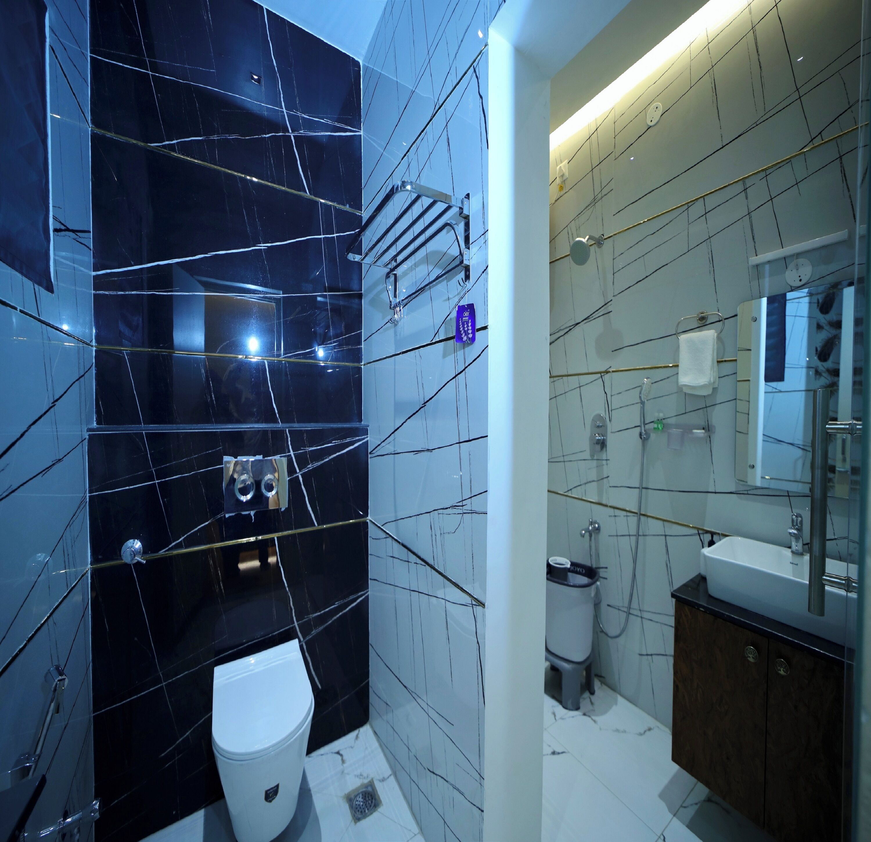 Une salle de bain moderne avec des murs en marbre noir, des toilettes blanches, un lavabo avec un miroir et un espace douche.