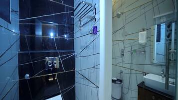 Une salle de bain moderne avec des murs en marbre noir, des toilettes blanches, un lavabo avec un miroir et un espace douche.