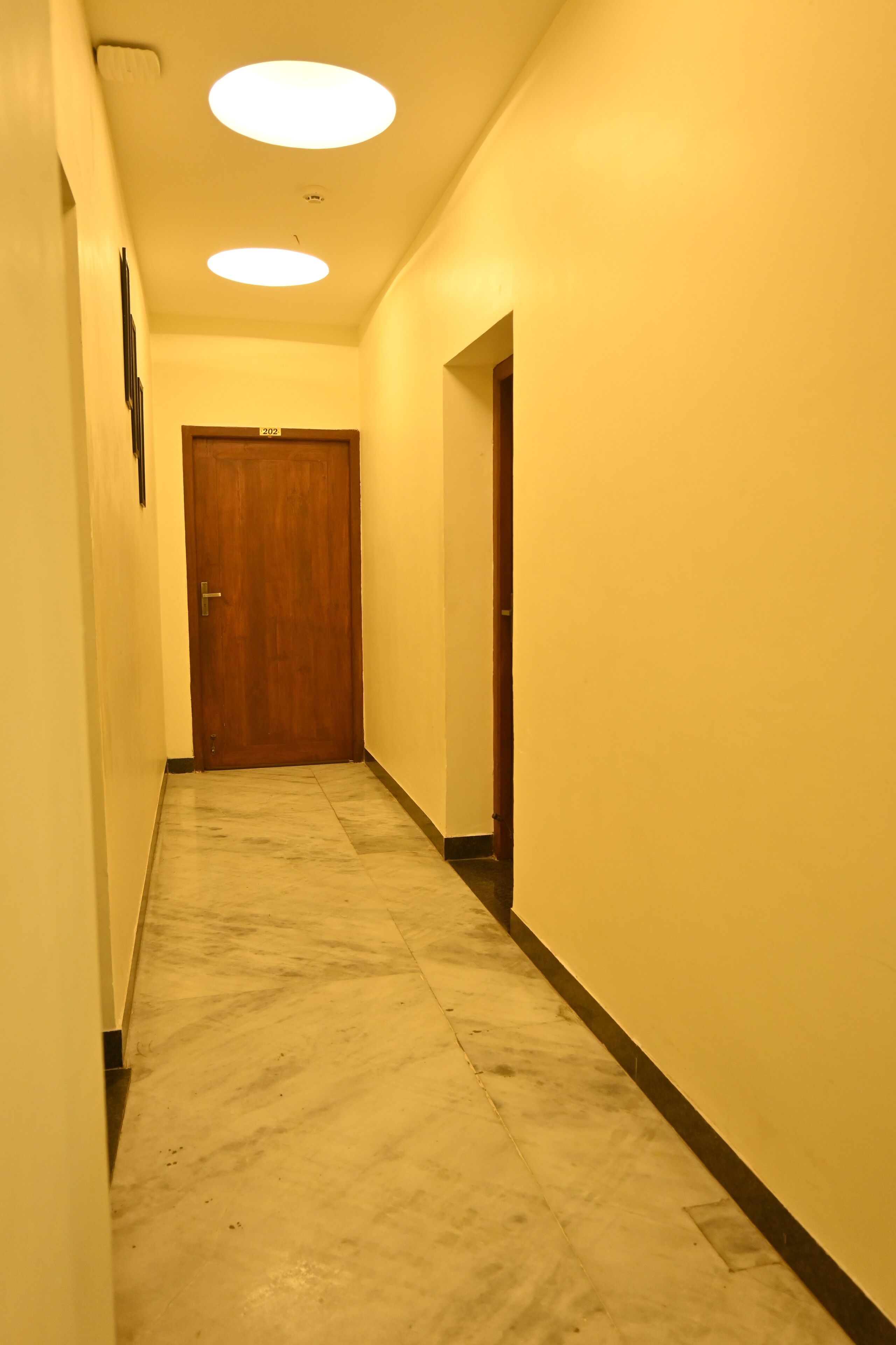A narrow hallway with a wooden door at the end, a marble floor, and recessed ceiling lights.