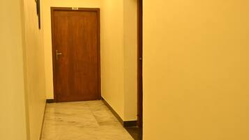 A narrow hallway with a wooden door at the end, a marble floor, and recessed ceiling lights.