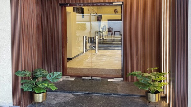 A modern entrance with vertical wooden slats, a glass door, and two potted plants. - Suthanthira Stay Inn (Thindukkal)