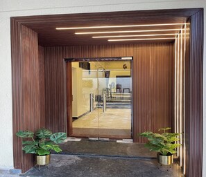 A modern entrance with vertical wooden slats, a glass door, and two potted plants. - Suthanthira Stay Inn (Thindukkal)