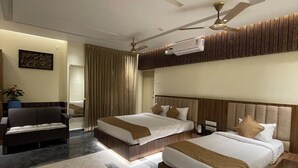 A hotel room with two beds, a sofa, a ceiling fan, an air conditioning unit, and a large window with curtains. - Suthanthira Stay Inn (Thindukkal)
