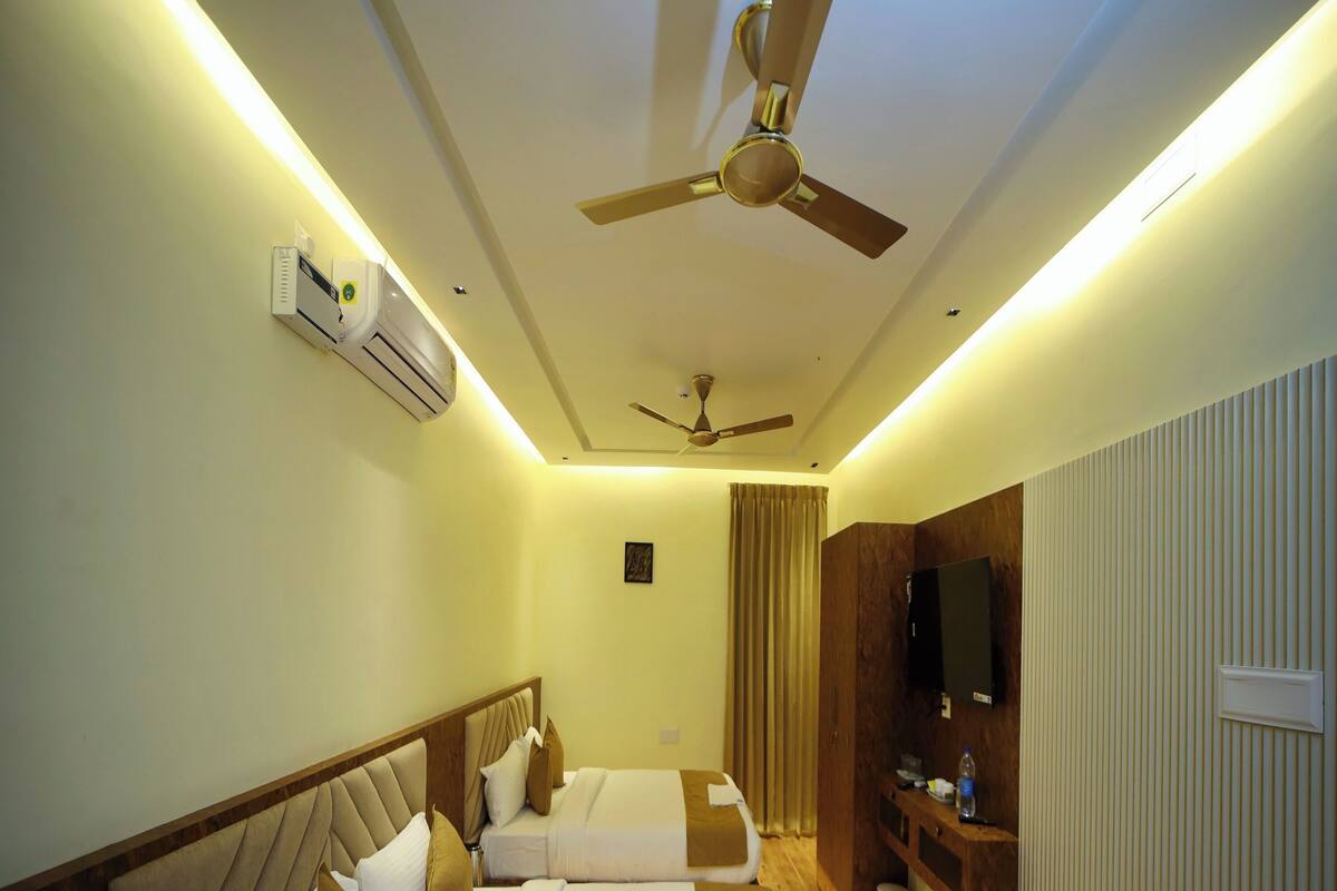 Une chambre d’hôtel avec deux lits, un ventilateur de plafond, un appareil de climatisation, une télévision et une commode en bois.