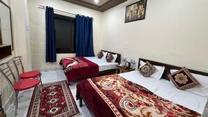 A hotel room with two beds, a sitting area with a red chair, a small table, and a decorative rug. - Hotel Royal Sainik (Bhatwari)