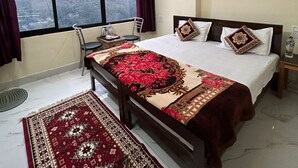 A bedroom with a large bed, a ceiling fan, a window with a view of mountains, and a rug. - Hotel Royal Sainik (Bhatwari)