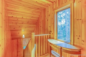 A wooden cabin interior with a window, a wooden staircase, and a small table.