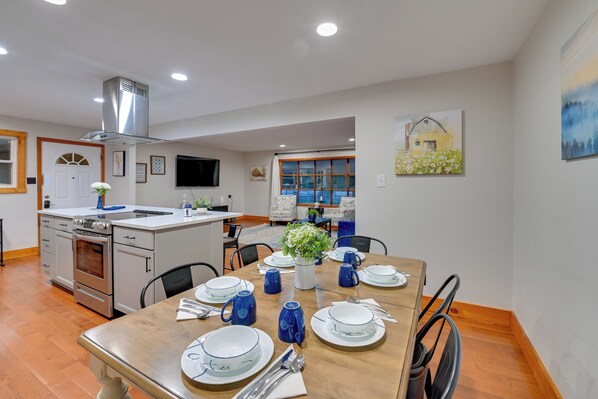 A modern kitchen with stainless steel appliances, a dining area with a wooden table set for four, and a large window with a view of a house. - Cabin Getaway Near Red River Gorge Recreation (Pine Ridge)
