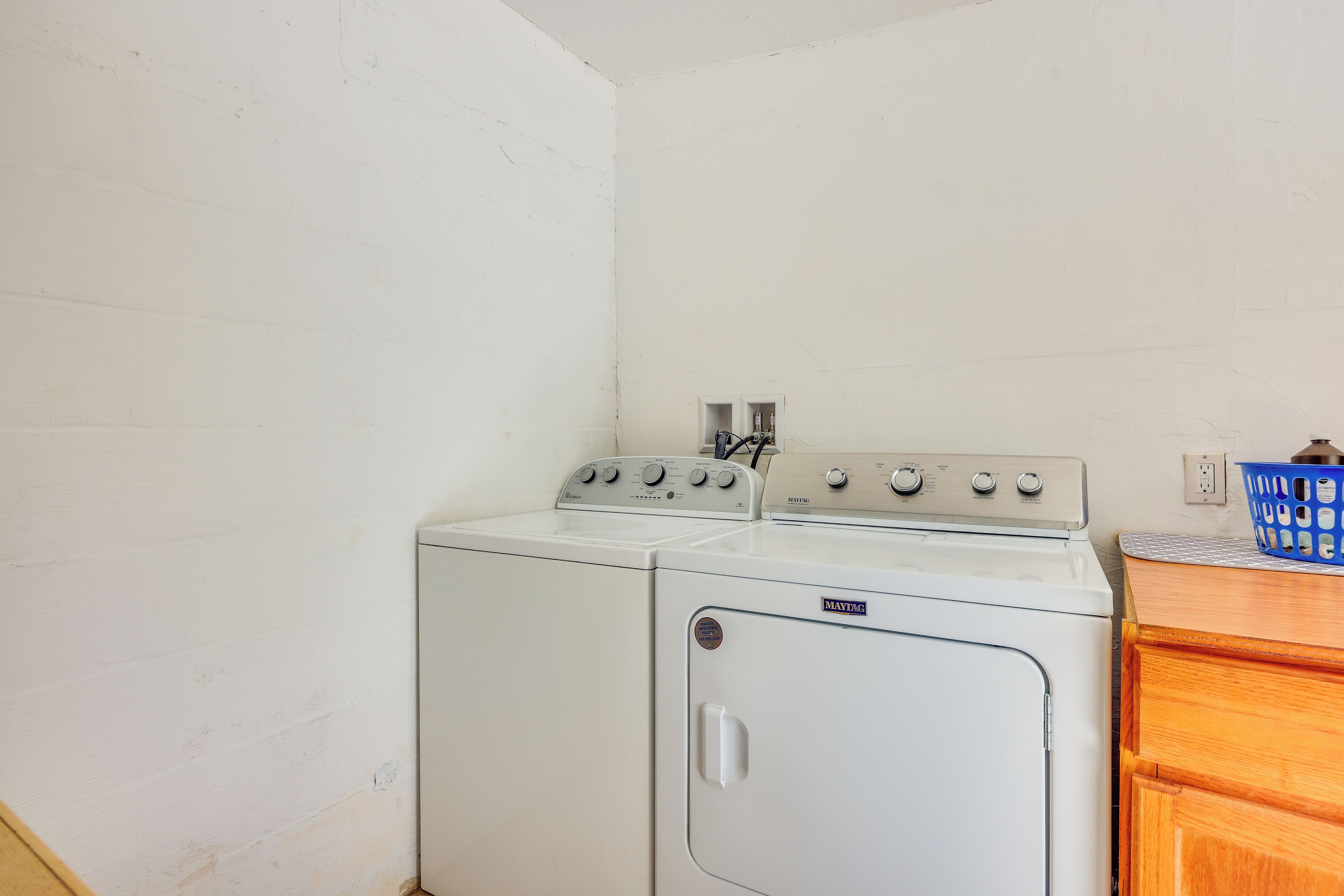 A laundry room with a white washer and dryer, wooden cabinets, and a blue basket on the counter.