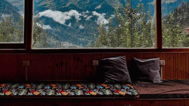 Interior de madera con un banco y un ventanal con vistas a un paisaje montañoso.