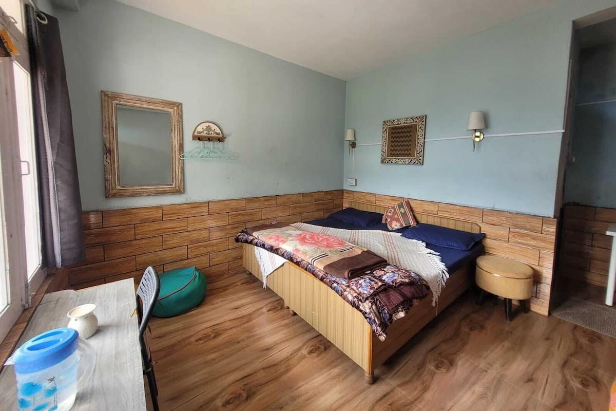 A bedroom with a wooden headboard, a bed with a floral bedspread, a bedside table with a lamp, and a window with curtains.
