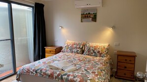 Een slaapkamer met een bed, nachtkastje, kledingkast, plafondventilator en raam met gordijnen.