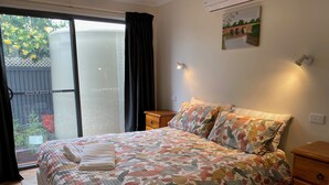 Een slaapkamer met een bed, nachtkastje, dressoir, raam met gordijnen en een wandairconditioner.