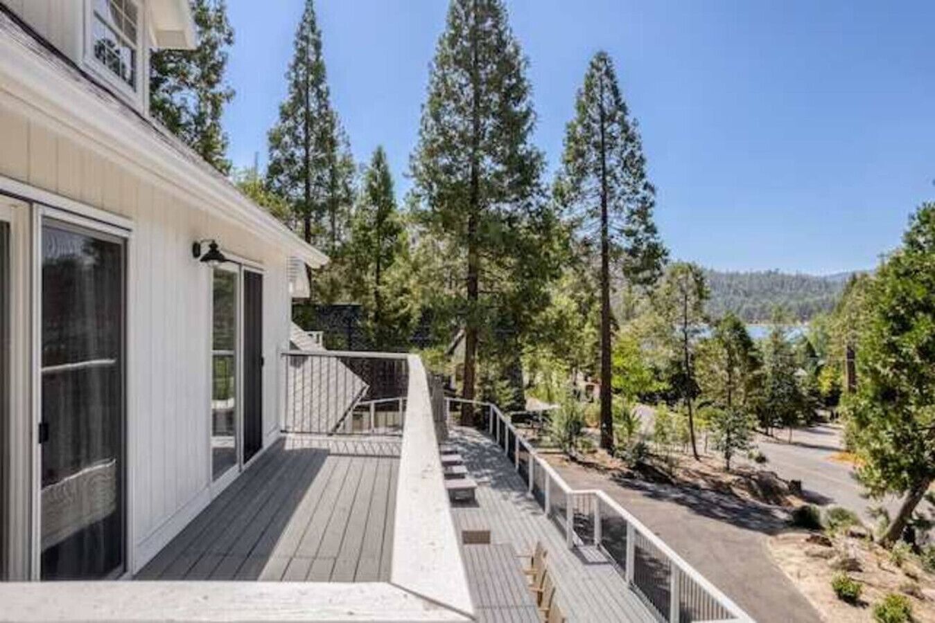 A wooden deck with a railing, a building with large windows, and tall trees in the background.