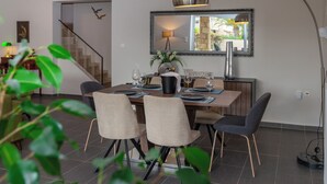 A dining area with a wooden table, four chairs, a lamp, and a mirror on the wall. - Villa Blu Mare Relax Place in Nafpaktos! (NAFPAKTOS)