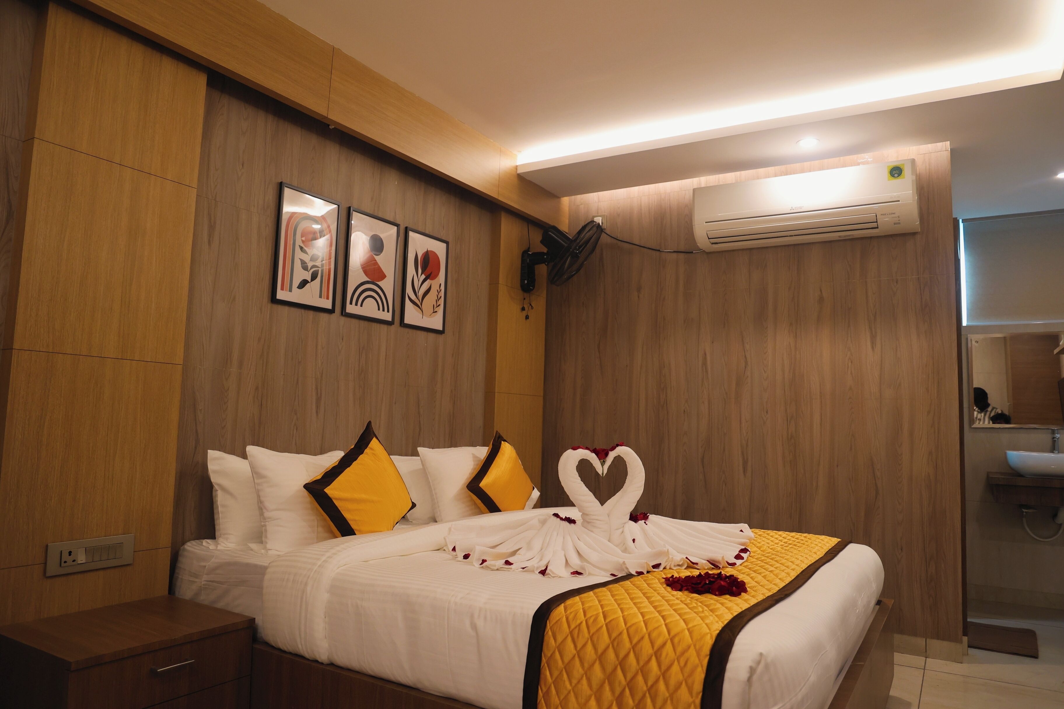 A hotel room with a bed, a nightstand, a wall-mounted air conditioner, and a bathroom visible through an open door.