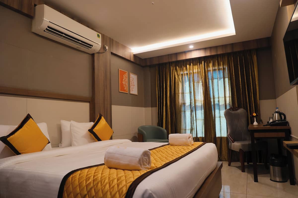 A hotel room with a large bed, a desk, a chair, an air conditioning unit, and a window with curtains.