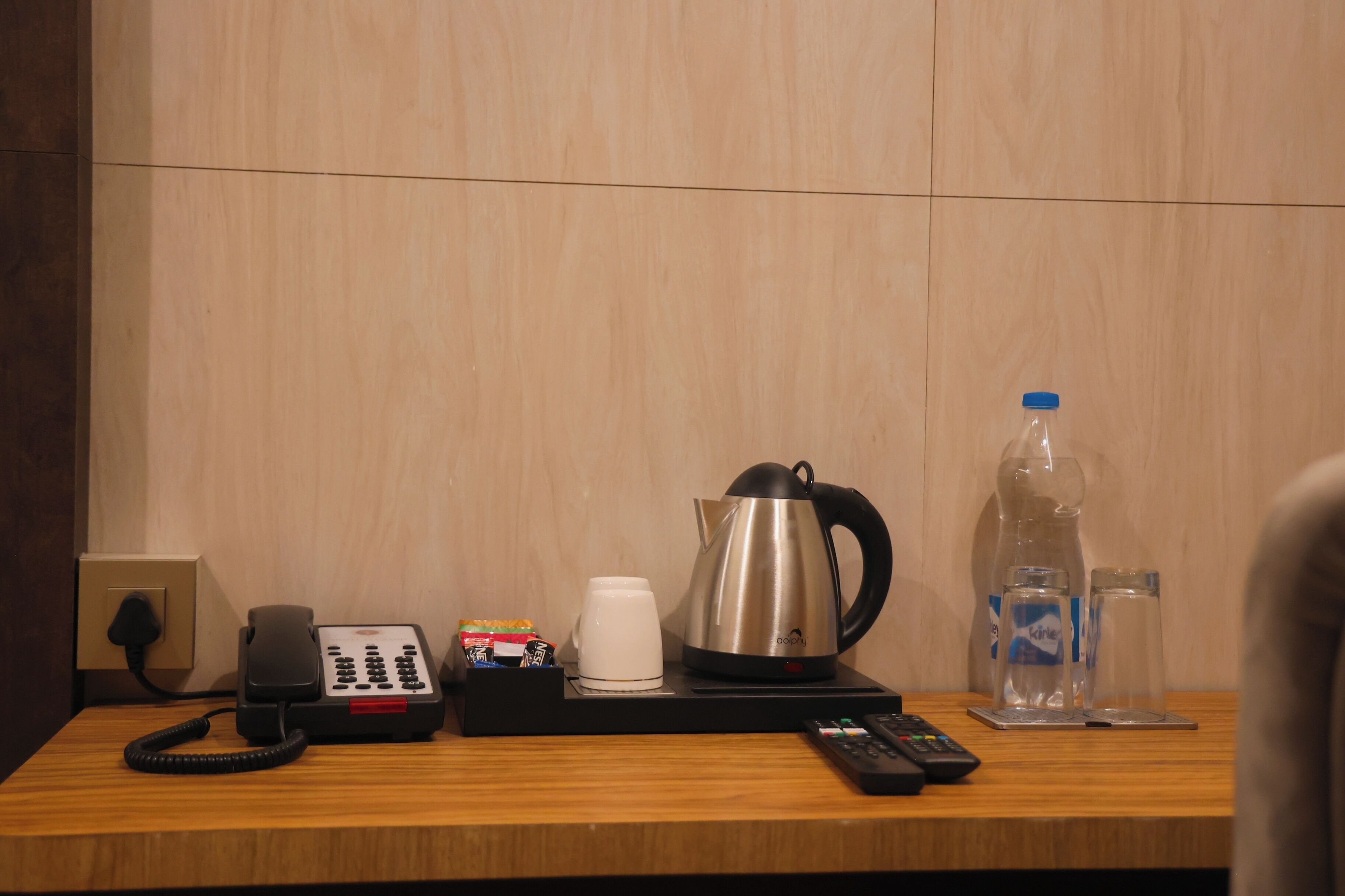 Escritorio de habitación de hotel con un teléfono, una cafetera, una botella de agua y un control remoto.